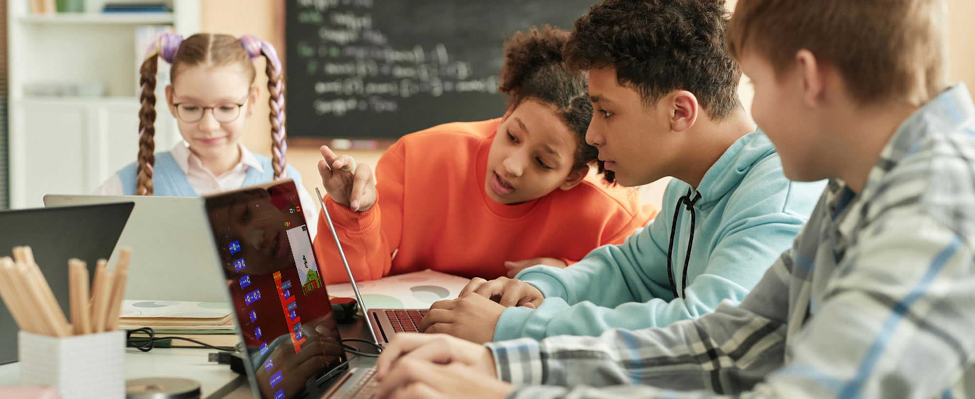 A diverse group of students gathered around a laptop, actively collaborating on their assignments.